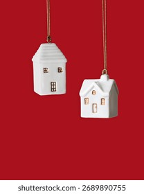 Minimal winter composition with two white ceramic house ornament hanging on red background. Simple Christmas decoration symbolizing home, warmth and holiday coziness. New Year colored Christmas decor
