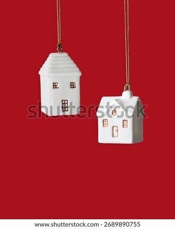 Minimal winter composition with two white ceramic house ornament hanging on red background. Simple Christmas decoration symbolizing home, warmth and holiday coziness. New Year colored Christmas decor