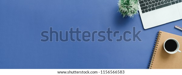 Minimal work space - Creative flat lay photo of\
workspace desk. Top view office desk with laptop, notebooks and\
coffee cup on blue color background. Panoramic banner background\
with copy space. 