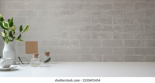 Minimal workspace with copy space and office supplies on white desk and grey brick wall background
