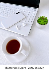 Minimal workspace featuring a blank keyboard, laptop, smartphone, wireless earbuds and a cup of coffee. Clean desk setup representing remote work, digital lifestyle and modern productivity.
