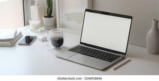 Minimaler Arbeitsbereich mit offenem Notebook-Bildschirm und Bürobedarf auf weißem Holztisch