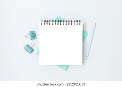 Minimal workspace with square notepad mockup and stationery on a blue background. Monochrome school concept with copyspace.