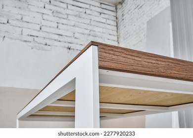 Minimalism style dining table with thin wooden table top of oak veneer on white metal legs in workshop closeup low angle view