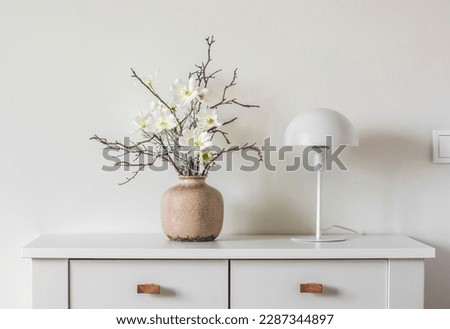 Minimalism style interior decor - flower arrangement in a ceramic vase and a white metal table lamp on a white table    