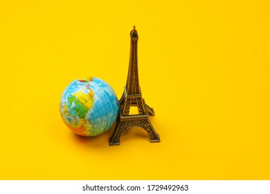 Minimalism Travel Still Life. Figurine Of The Eiffel Tower, Globe On A Yellow Background.