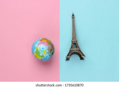 Minimalism Travel Still Life. Figurine Of The Eiffel Tower, Globe On Pink Blue Pastel Background.