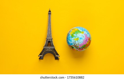 Minimalism Travel Still Life. Figurine Of The Eiffel Tower, Globe On A Yellow Background. Top View