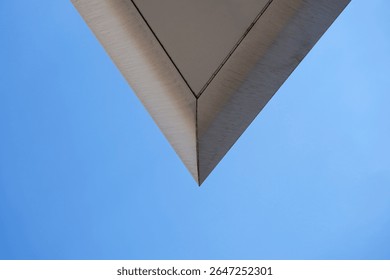 Minimalist architectural composition with sharp triangular corner of modern building against clear blue sky, symbolizing precision and abstract geometry.

