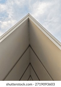 Minimalist architectural composition of a sharp white building corner pointing upwards against a cloudy sky, abstract geometry.