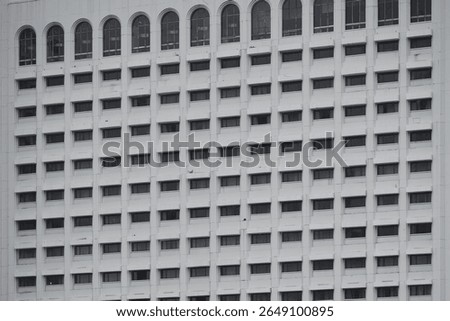 A minimalist architectural pattern of repeating windows on a white building facade. The symmetrical grid and arched windows at the top create an abstract, textured background.