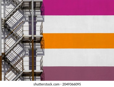 Minimalist architectural photo of a building facade with colorful horizontal stripes and fire escape stairs. 