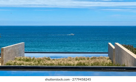 Minimalist architectural view of an infinity pool looking out to the vast ocean with a lone boat on the horizon