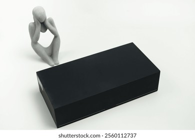 Minimalist artwork featuring a sculpture in a pensive pose beside a sleek black rectangular box on a white background. The concept evokes simplicity, modern design, and symbolic contemplation - Powered by Shutterstock