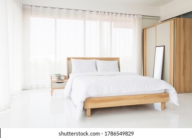 Minimalist bedroom interior with white sheet bed, blanket and pillows all white colors on double wood bed frame, side bed table and The closet. Nice and clean bedroom design concept. - Shutterstock ID 1786549829