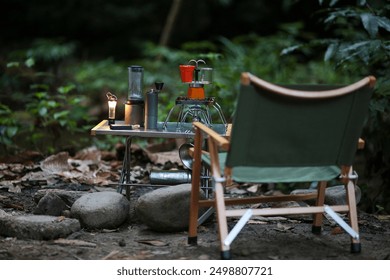 Minimalist camping coffee setup with a portable coffee maker, gas stove, and lantern on a table, set in a forest with a green camping chair. - Powered by Shutterstock