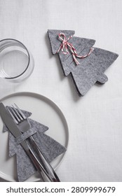 Minimalist Christmas table setting featuring a simple felt fir tree decoration, polished silverware, and linen on a rustic surface.