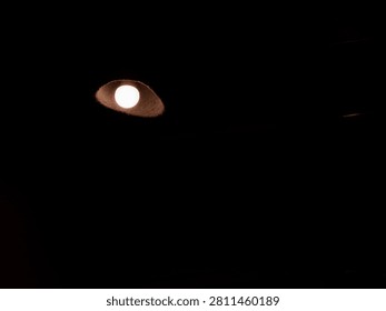 A minimalist close-up of a single ceiling light shining through a circular opening in a dark interior. The high-contrast composition emphasizes light, shadow, and negative space, making it suitable for concepts of illumination, solitude, mystery, and modern architectural details.