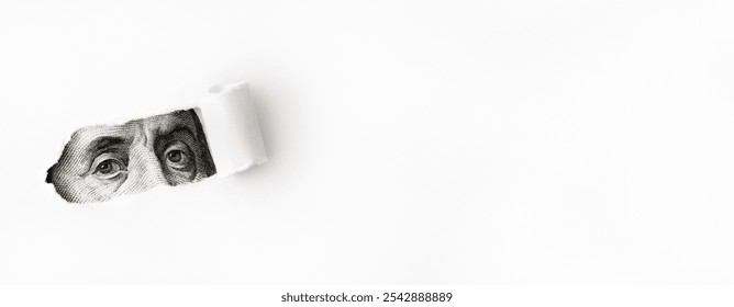 A minimalist composition with a close-up of Benjamin Franklin's eyes from a U.S. one-hundred-dollar bill, visible through, torn section on a white background. Blank space with torn paper section. 