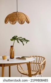 Minimalist composition of elegant kitchen space with round table, rattan chair, vase with leaf, pedant lamp and personal accessories. Minimalist home decor. Beige wall. Template.	