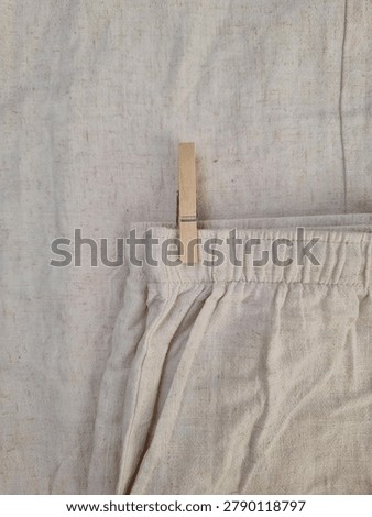 Minimalist composition featuring pants hanging with a clothespin against a calm, soft summer-toned background. The image reflects simplicity, quiet domestic life, and a relaxed seasonal mood with clean design and natural light.