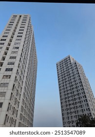 A minimalist composition featuring two towering apartment buildings reaching for the clear blue sky. The clean lines and geometric shapes of the buildings create a sense of modern urban architecture.