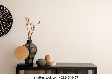 Minimalist composition of living room interior with copy space, black commode, vase with dried flowers, decoration on the wall and stylish personal accessories. Home decor. Template. 