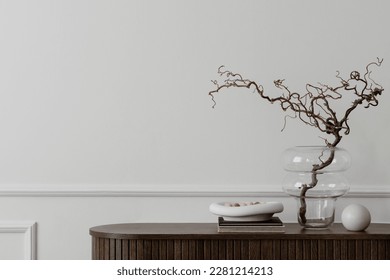 Minimalist composition of living room interior with copy space, wooden sideboard, glass vase with branch, bowl, ball sculpture and personal accessories. Home decor. Template. 