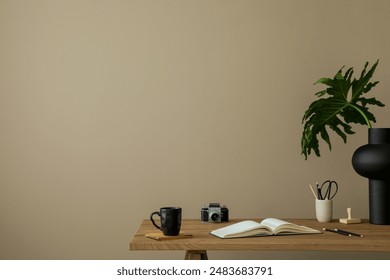 Minimalist composition of workplace interior with copy space, wooden desk, books, camera, black cup, pencils, stylish vase with leaves, brown wall and personal accessories. Home decor. Template.