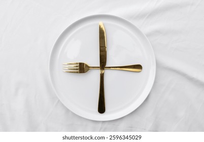 A minimalist dining scene showcasing an empty ceramic plate set with a fork and knife, placed on a white tablecloth for a clean and sophisticated look.