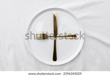 A minimalist dining scene showcasing an empty ceramic plate set with a fork and knife, placed on a white tablecloth for a clean and sophisticated look.
