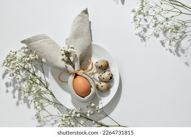 Minimalist Easter aesthetic table setting, egg decorated with bunny ears napkin on a plate. Neutral floral background with copy space. Holiday spring template or banner design