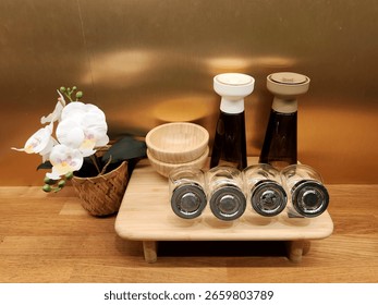 A minimalist and elegant collection of kitchenware, featuring spice jars, a small wooden bowl, and a graceful white orchid, arranged on a light wooden tray. The image captures a serene, organized kitc