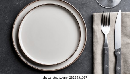A minimalist and elegant table setting featuring a clean white plate, a silver fork, and a knife, arranged on a dark textured surface.