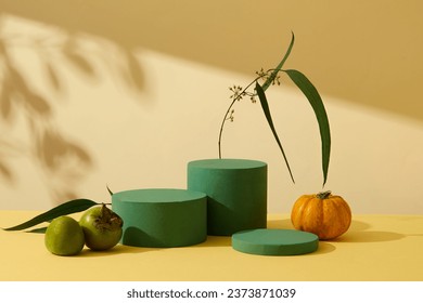 Minimalist empty display product presentation scene with Autumn theme. Three green cylinder podiums displayed on yellow background with pumpkin and green persimmons. Front view