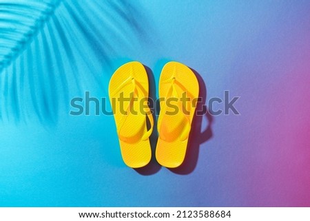 Minimalist flat lay photo of pair of beach flip-flops with copy space. Yellow flip-flops on the blue background with palm tree shadow.