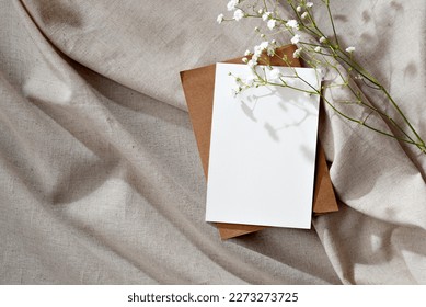 Minimalist floral wedding invitation or greeting card, postcard template, blank paper card and flowers on a beige neutral linen background