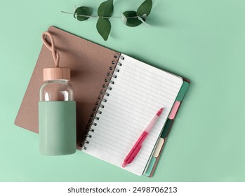 Minimalist Green Workspace with Open Notebook, Pen, Eco-Friendly Water Bottle, and Leaves. - Powered by Shutterstock