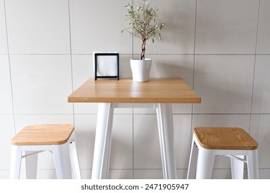 minimalist high table with two stools, small plant, photo frame, modern setting. 
