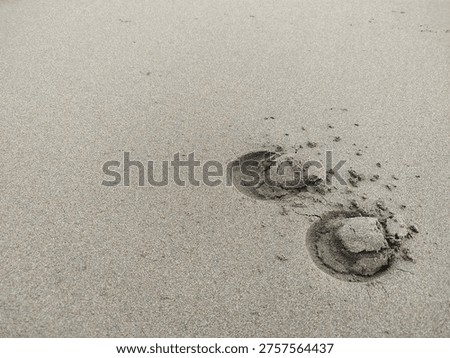 A minimalist and high-angle shot featuring two distinct circular footprints on a vast, textured sand surface. The large negative space on the left side makes it an ideal background for text or graphic overlays. Perfect for concepts of travel, journey, solitude, or coastal nature.