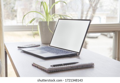 Minimalist Home Office Set Up, Laptop, Cell Phone, Notebook, Pen And A Plant On A Desk Against A Window With  Bright Natural Light