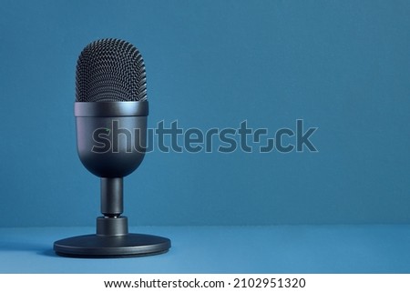 Minimalist image of a modern and elegant black design microphone for streaming and gaming on a colorful blue background with texture and copy space. Technology and entertainment.