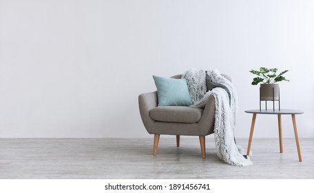 Minimalist interior of bedroom, cabinet or living room. Gray modern armchair with blue pillow and soft blanket, on table pot with plant, home design with light wall in scandinavian style, panorama
