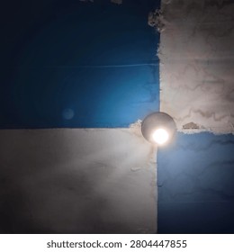 Minimalist interior ceiling with a glowing light bulb against blue and white painted walls. Abstract architectural composition featuring geometric shapes, light, shadow, and textured surfaces in a residential space.