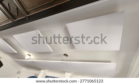Minimalist interior ceiling with rectangular white acoustic panels installed for sound absorption and noise reduction. Clean modern design with soft lighting fixtures, visible wooden ceiling detail, and suspended panels arranged in a geometric layout. Suitable for office, studio, or commercial space focused on acoustics and comfort.