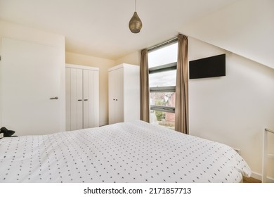 Minimalist Interior Design Of A Small Bedroom With A Soft Bed, White Cabinets, Windows And A Small TV On A White Wall