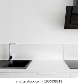 Minimalist kitchen with white countertop, furniture and wall tiles and black sink, induction hob and exhaust hood - Powered by Shutterstock