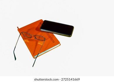 The minimalist layout of three objects on a white background, an orange cover notebook, a smartphone and a pair of metal-framed glasses creates a concise and modern study atmosphere
                               