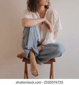 Minimalist Lifestyle. Pretty Woman with Curly Hair Sitting Cross-Legged on Wooden Stool in Casual Natural Pose - Powered by Shutterstock