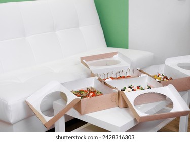 In a minimalist office with white and green walls, a set of snack boxes sit on a white table for a team party. Horizontal photo - Powered by Shutterstock